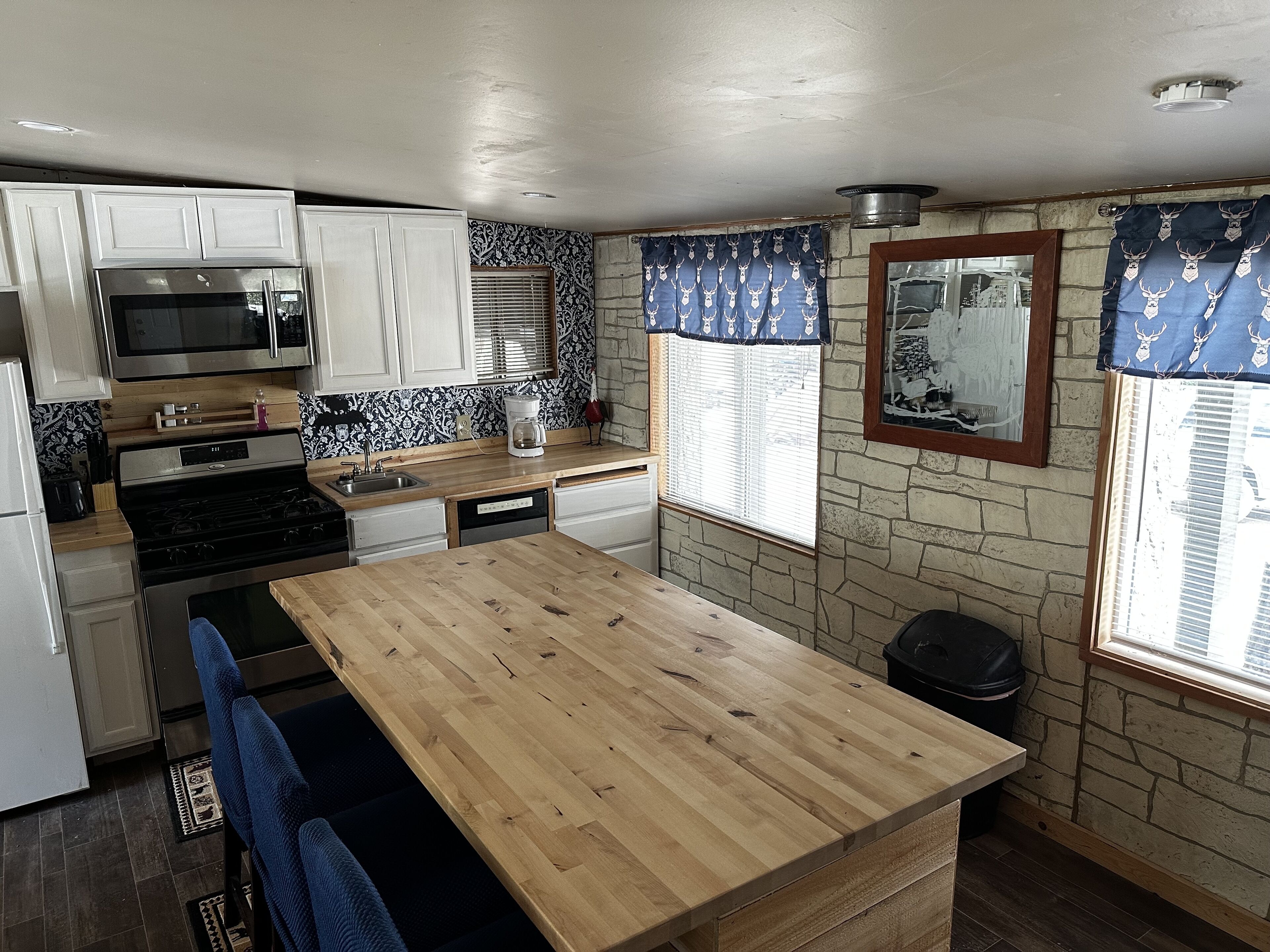 A compact kitchen with white cabinets, a stainless steel refrigerator, a microwave, a stove, and a wooden island.