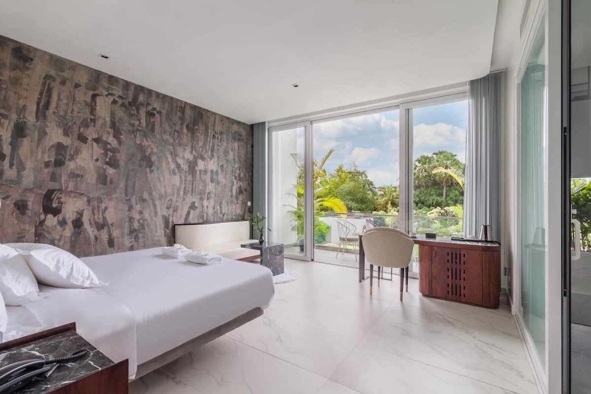 Quarto moderno com uma cama grande, uma escrivaninha e varanda com vista para o verde.