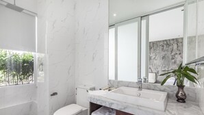 A modern bathroom with a large mirror, white marble walls, a white toilet, a bathtub, and a marble vanity with a sink and a plant. - Enjoy Boutique Hotel & Restaurat (Siem Reap)