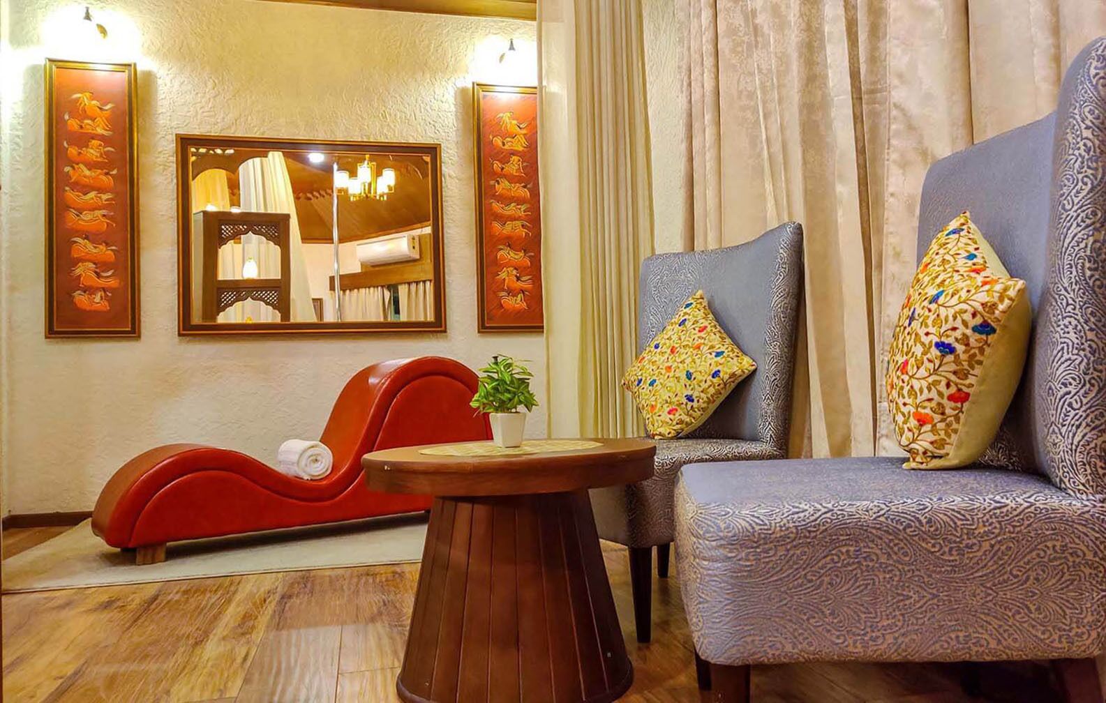 A room with a red massage chair, a grey sofa with patterned cushions, a wooden coffee table, and a wall-mounted mirror.
