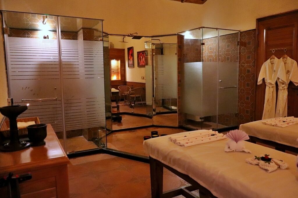 Une salle de spa équipée de deux tables de massage, d’un miroir et d’un petit coin salon avec une chaise et une table.