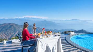 A dining table with food and drinks, set against a mountainous backdrop.
