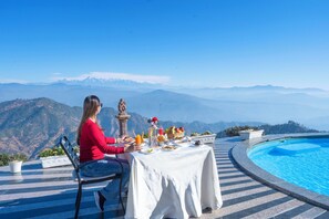 A dining table with food and drinks, set against a mountainous backdrop.