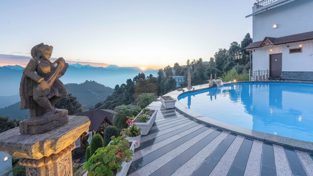 A stone statue on a ledge overlooking a pool with a view of mountains. - Vatsyayana Resorts (Salt)