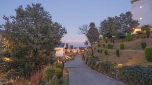 A pathway leading to a building with multiple windows and a well-maintained garden with trimmed bushes and trees. - Vatsyayana Resorts (Salt)