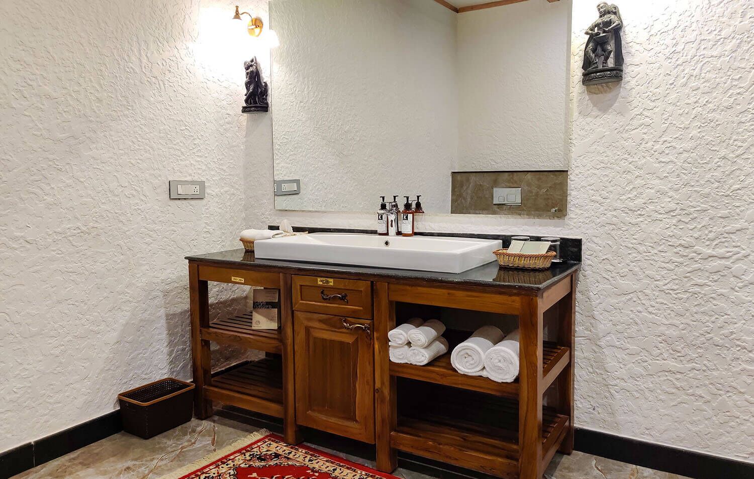 A bathroom with a wooden vanity, a large mirror, and a sink. There are towels and toiletries on the vanity.