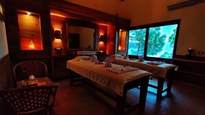 A cozy room with two beds, a table with a candle, and a large window with a view of trees. - Vatsyayana Resorts (Salt)