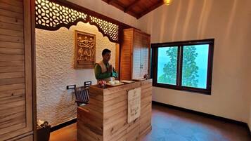 A reception desk with a wooden finish, a decorative wall, and a window with a view of trees.