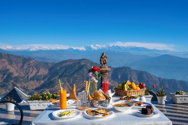 Une table dressée avec de la nourriture et des boissons sur une terrasse offrant une vue sur la montagne.