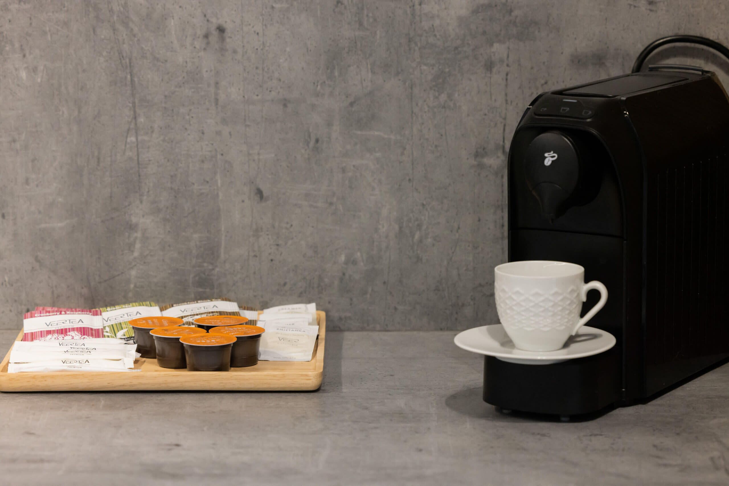 Una cafetera, una bandeja con cápsulas de café y una taza sobre una mesa.