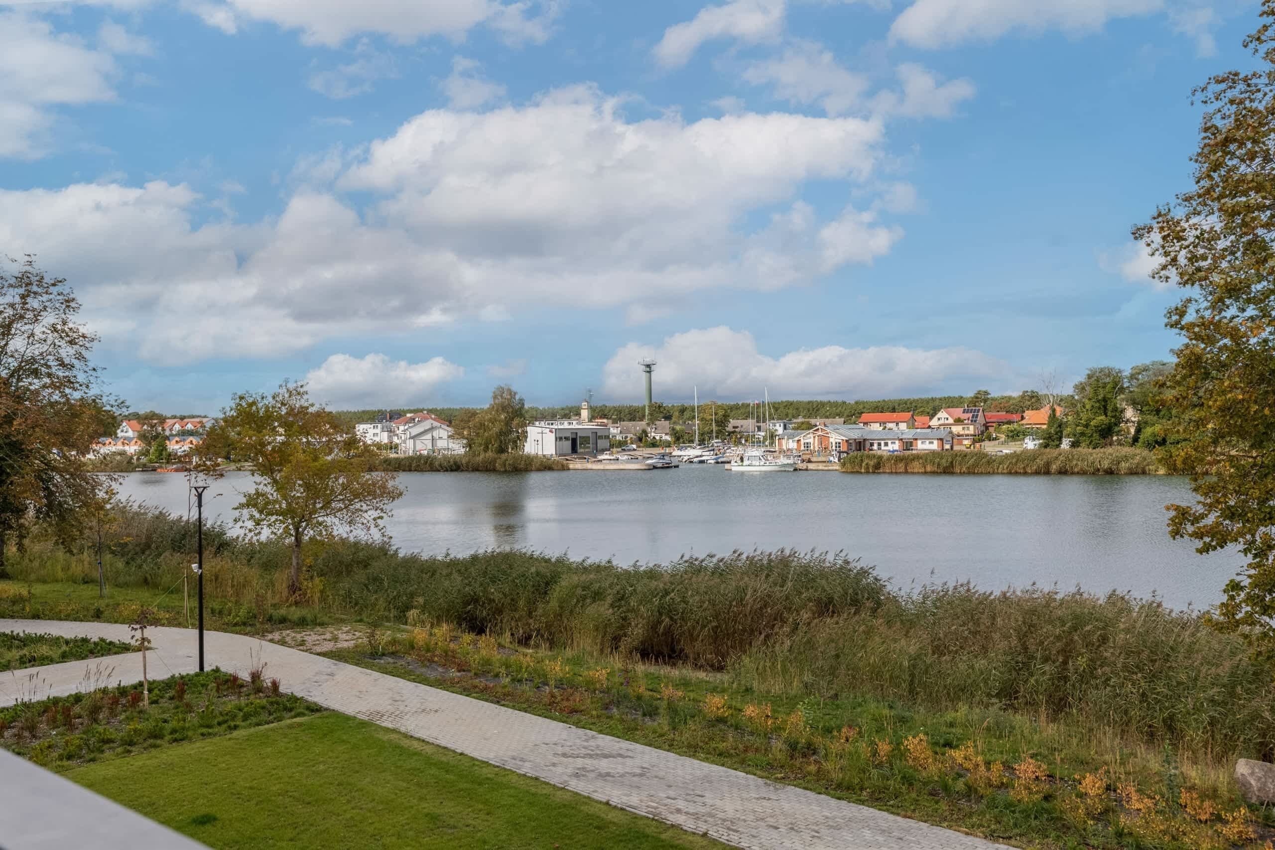 A riverside view with a paved walkway, buildings, and a small dock.