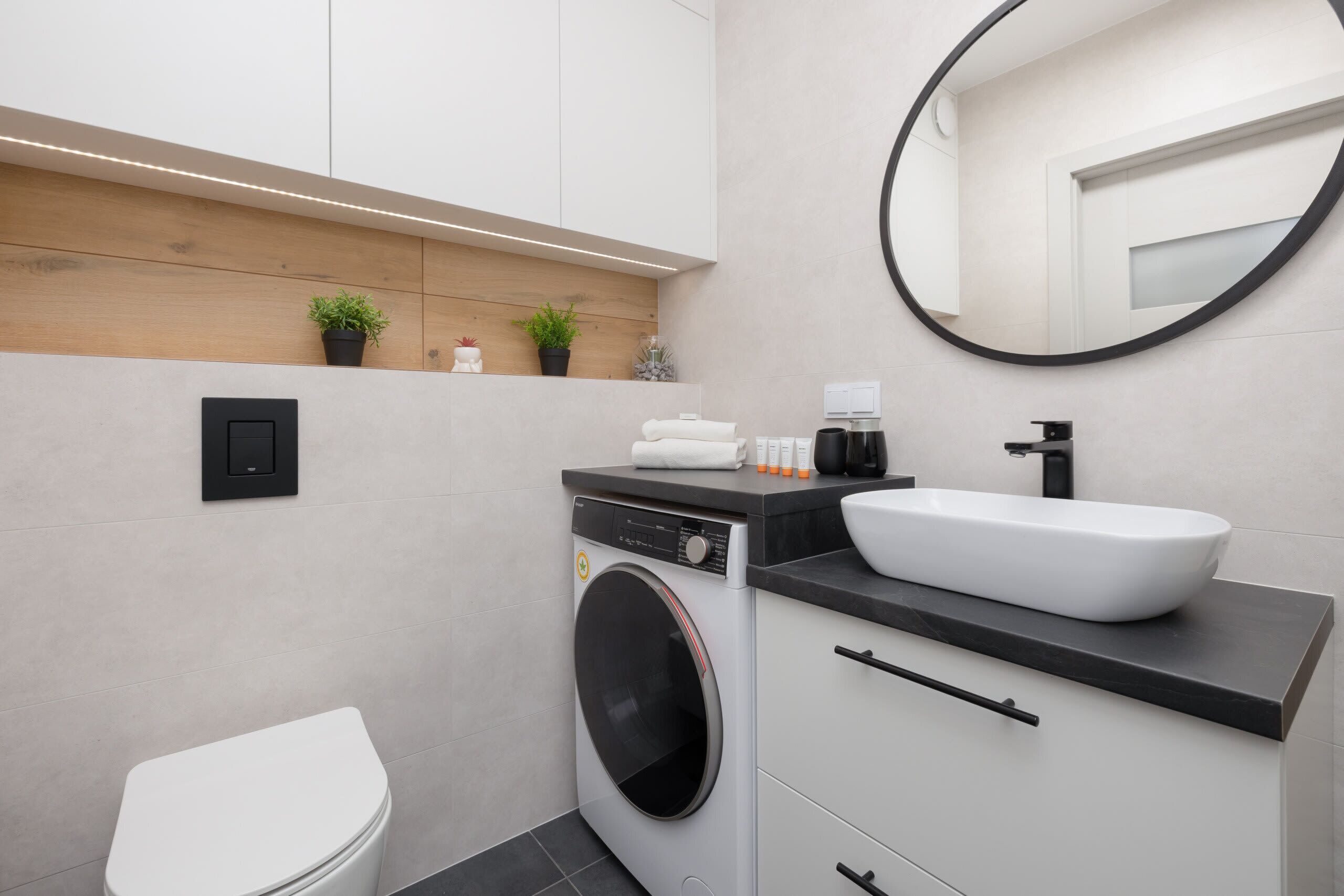Une salle de bain moderne équipée d’un lave-linge intégré, d’un lavabo avec un grand bac et d’un miroir rond.