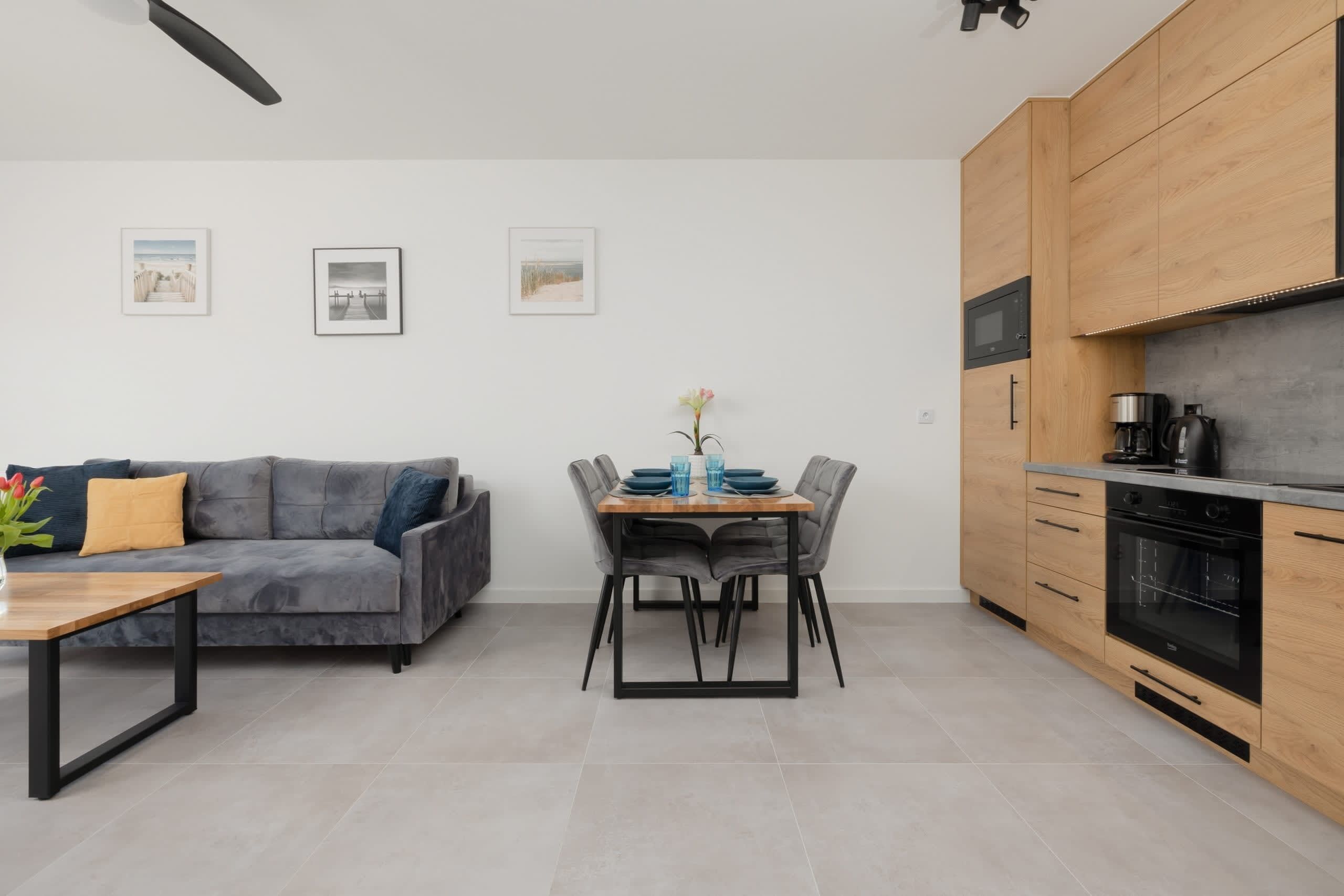 A modern kitchen with wooden cabinets, a built-in oven, and a dining area with a gray sofa and a table.