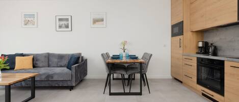 A modern kitchen with wooden cabinets, a built-in oven, and a dining area with a gray sofa and a table.
