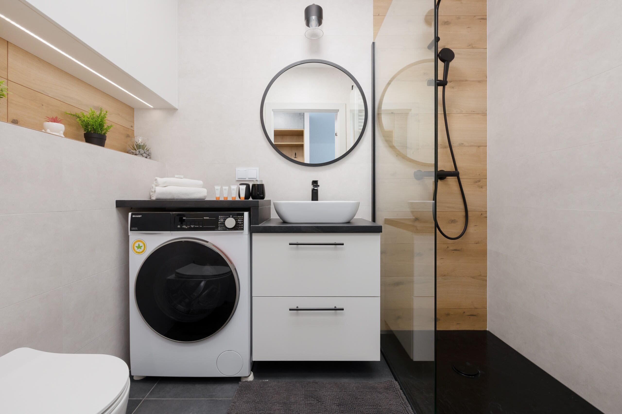 Une salle de bain moderne équipée d’un lave-linge, d’un évier et d’une douche.