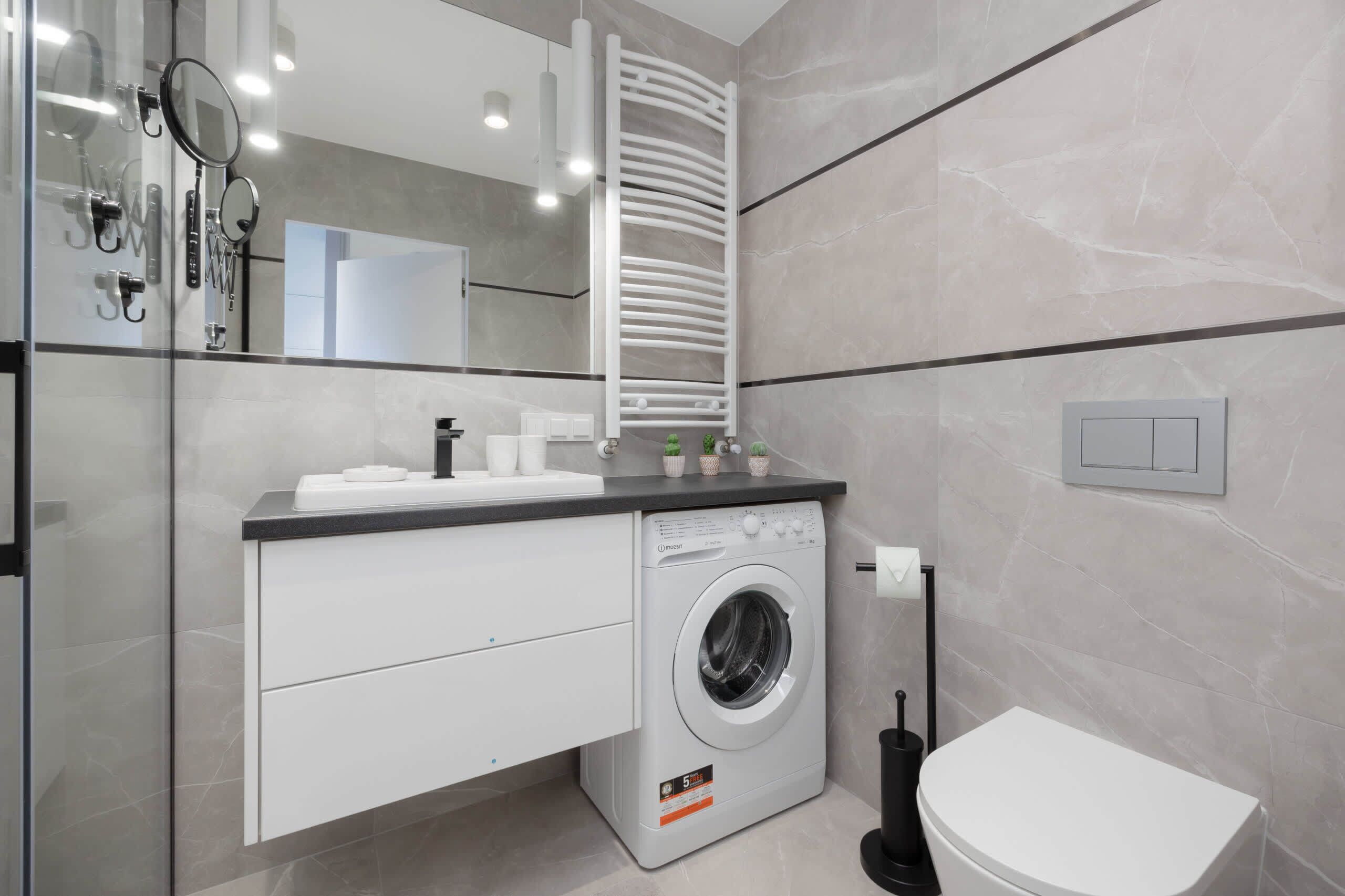 Un baño moderno con lavadora integrada, inodoro y barra para toallas.