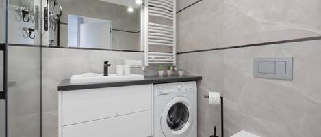 Un baño moderno con lavadora integrada, inodoro y barra para toallas.