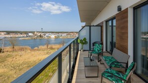 Un balcón con vista a un lago, muebles de mimbre y una planta en maceta.