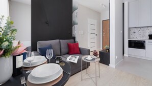 A modern living room with a grey sofa, a small round table, and a dining area with plates and glasses. - Tasteful Studio | Balcony | Workspace (Kraków)