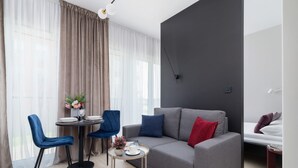 A modern living room with a grey sofa, blue chairs, a small round table with a vase of flowers, and a bed with a red pillow. - Tasteful Studio | Balcony | Workspace (Kraków)