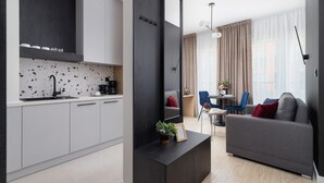 A modern kitchen with white cabinets, a black countertop, and a backsplash with speckled tiles. There is a dining area with a gray sofa, blue chairs, and a small table. - Tasteful Studio | Balcony | Workspace (Kraków)