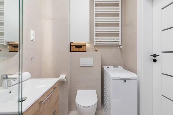 A modern bathroom with a glass shower enclosure, a white toilet, a built-in sink, and a towel rack.