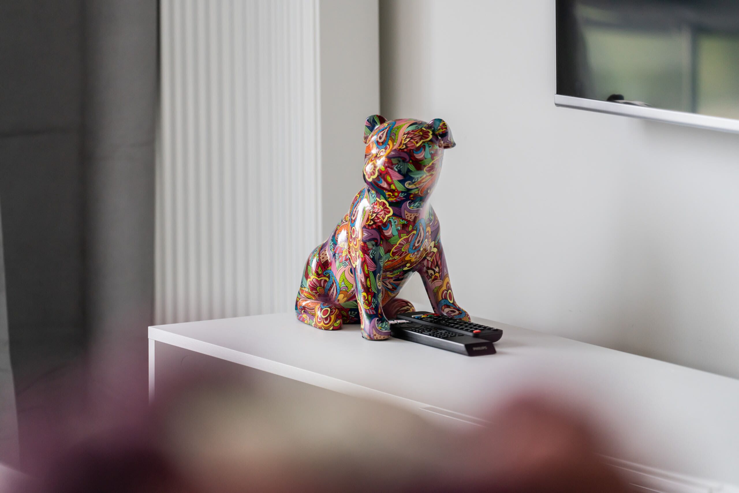 Una figura de oso de colores sobre una estantería blanca, con un control remoto a su lado.