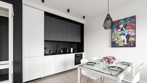 A modern kitchen with white cabinets, a black countertop, and a dining area with a glass table and white chairs. - Sunny Apartment with Balcony | Parking | Lake View (Poznan)