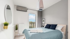 A modern bedroom with a large bed, a window with a view, a bedside table, and a wall-mounted air conditioner. - Sunny Apartment with Balcony | Parking | Lake View (Poznan)