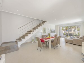 A spacious living area with a dining table set for four, a staircase, and a view of the outdoors.