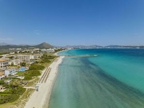 A coastal resort with a long sandy beach, clear turquoise waters, and a mountain in the background.