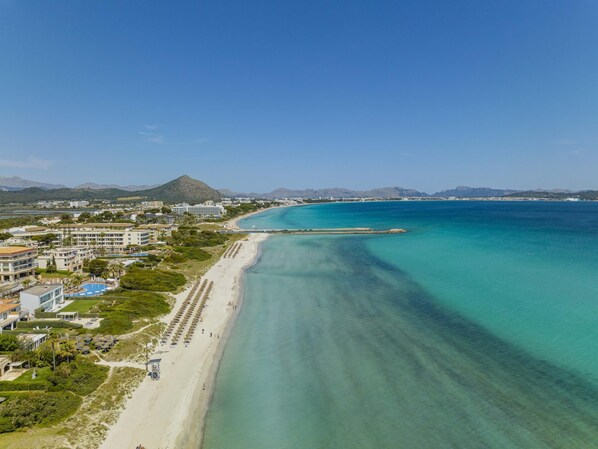 A coastal resort with a long sandy beach, clear turquoise waters, and a mountain in the background.