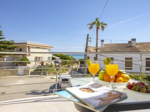 A balcony with a table set for breakfast, overlooking a coastal road and buildings.