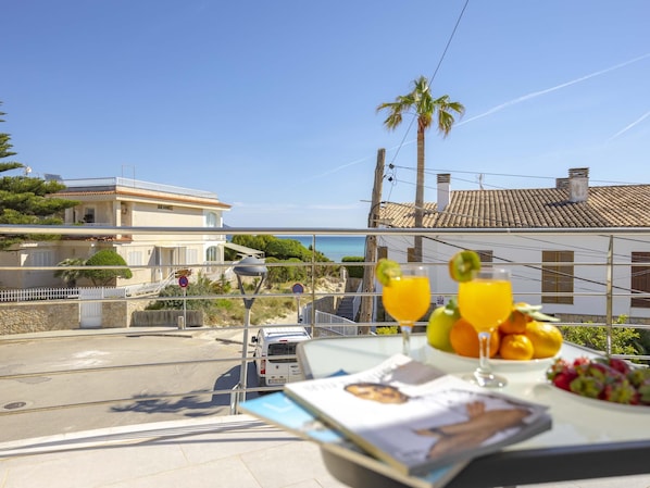 A balcony with a table set for breakfast, overlooking a coastal road and buildings.