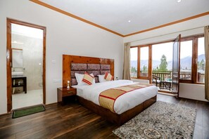 A spacious bedroom with a large bed, wooden headboard, and a view of mountains through the balcony.