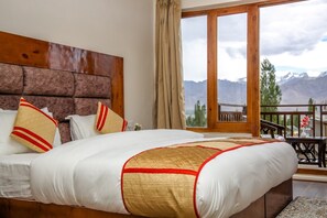 A bedroom with a large bed, a wooden headboard, and a view of mountains through a glass door.