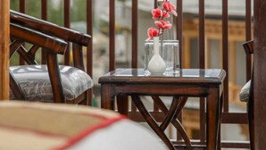 A balcony with a view of mountains, a wooden chair, a small table with a vase of flowers, and a glass of water.