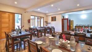 A spacious dining area with multiple tables and chairs, a kitchen in the background, and a view of the outside.