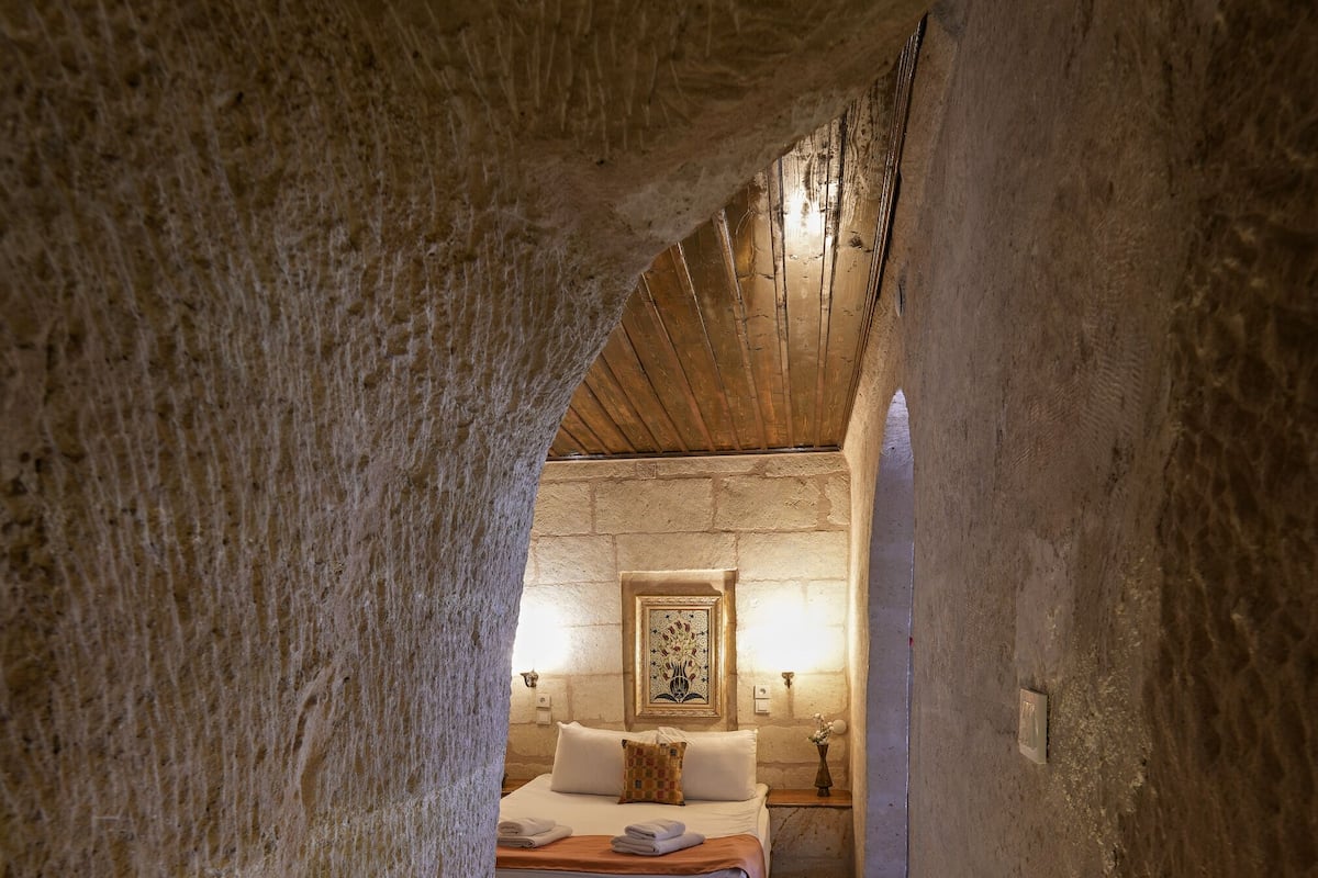 Un estrecho pasillo que conduce a un dormitorio con cama, lámparas de noche y una alfombra estampada.