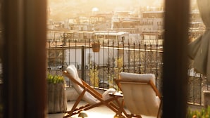 Un balcón con dos sillones de descanso y una mesa, con vistas a un paisaje urbano que incluye edificios y una valla.