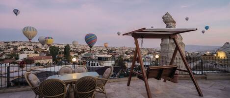 Eine Terrasse mit Korbmöbeln und einer Schaukel mit Blick auf eine Stadtlandschaft, in deren Himmel Heißluftballons schweben.