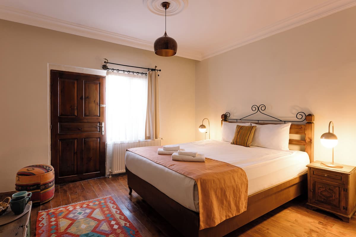 Un dormitorio ordenado con una cama de madera, lámparas de noche, una mesita de noche de madera, una alfombra colorida y una puerta de madera.