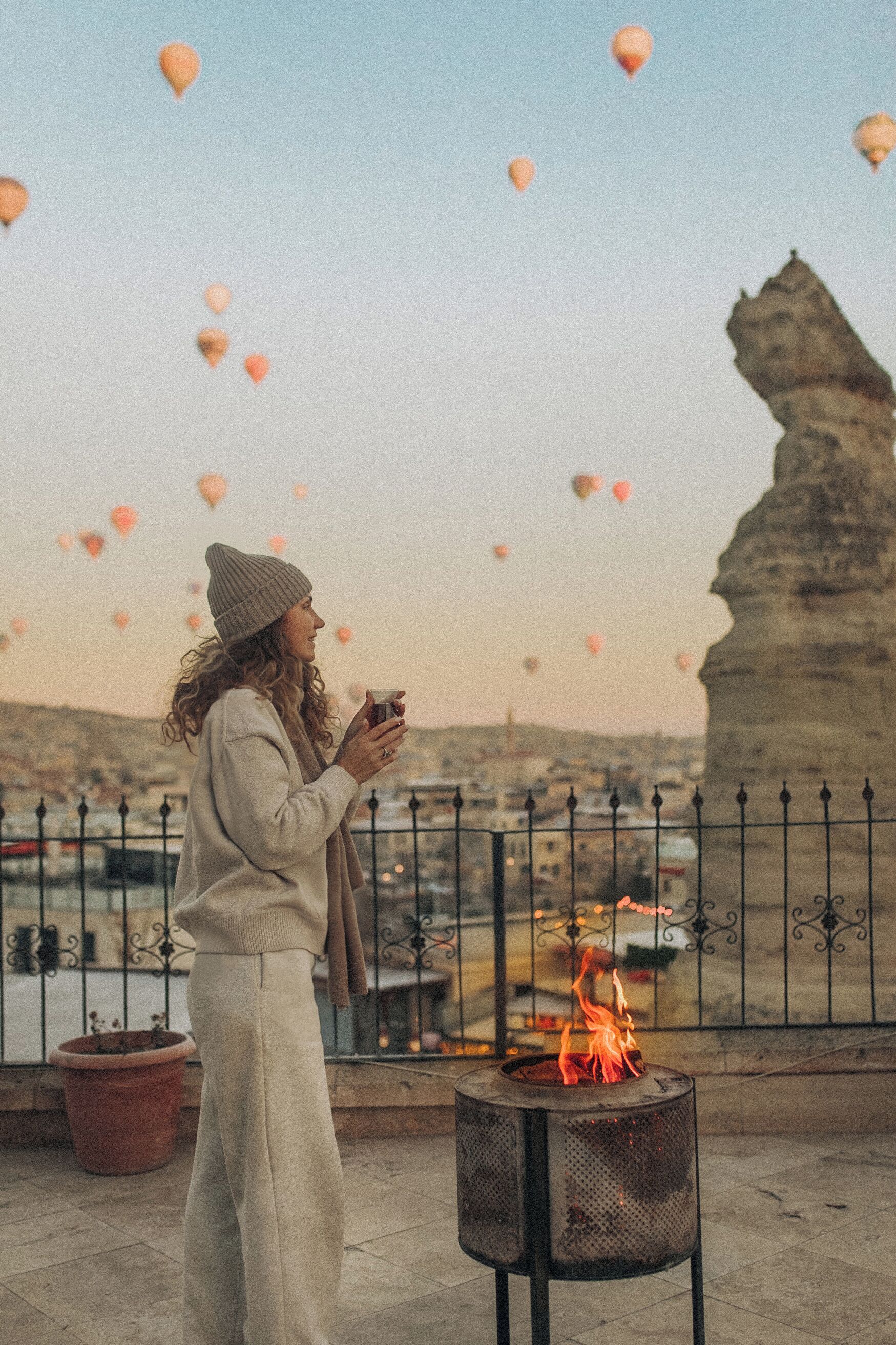 Una persona in piedi su un balcone con un elemento decorativo a fuoco, con vista su un panorama urbano e una formazione rocciosa.