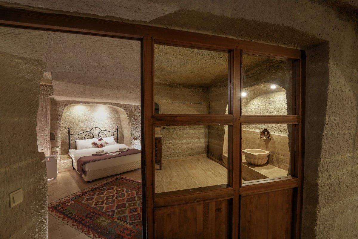 Un dormitorio rústico con cama, ventana de madera y pared de piedra.