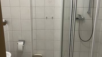 Baño con inodoro, cabina de ducha y cubo de basura.