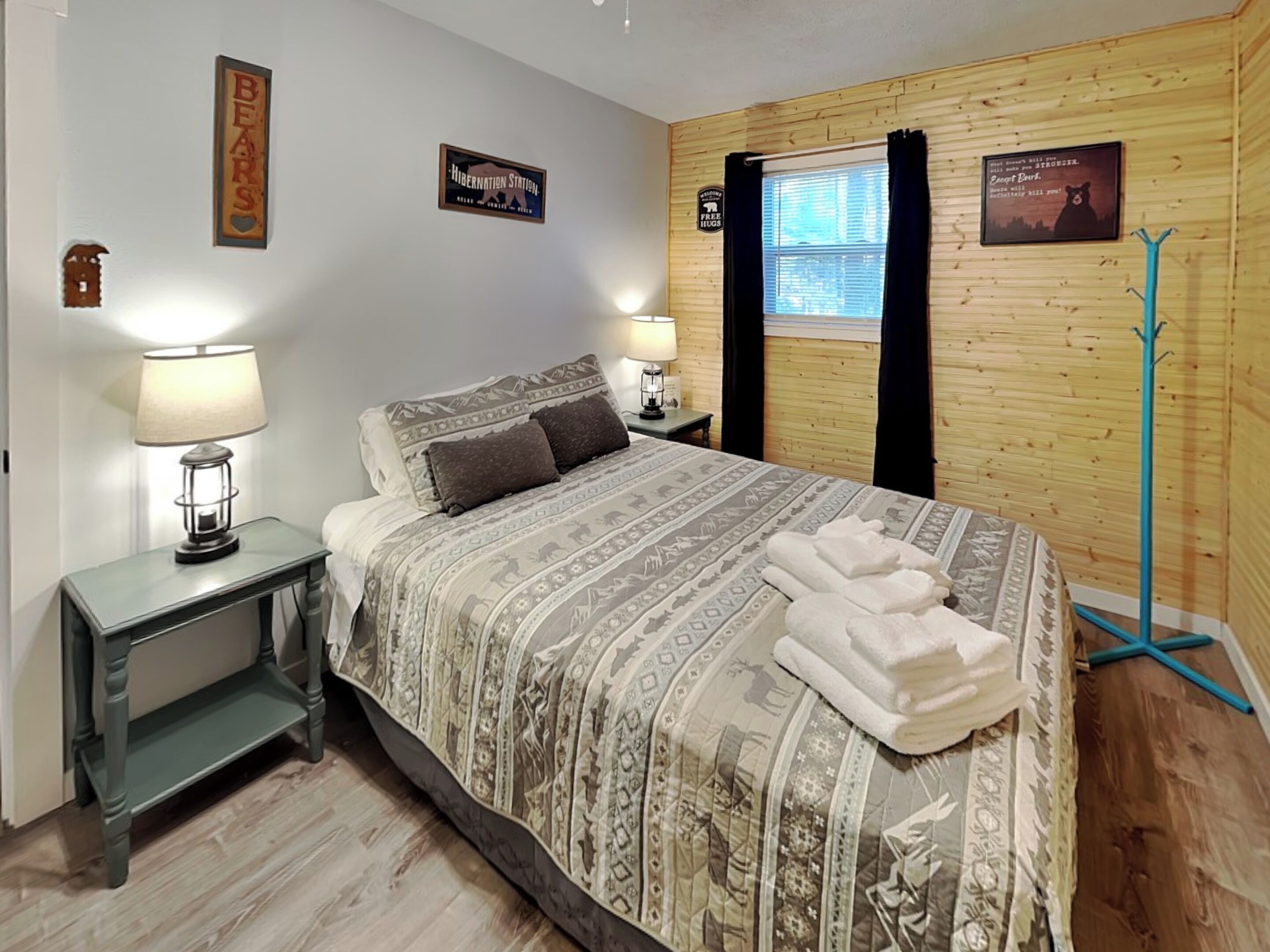 A bedroom with a bed, two bedside tables, a window with curtains, and a coat rack.