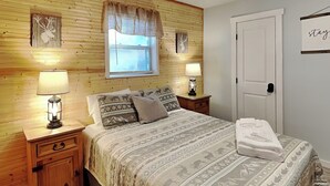 Une chambre à coucher avec une tête de lit en bois, un lit avec une literie à motifs, deux lampes de chevet, une table de chevet et une porte avec une pancarte.