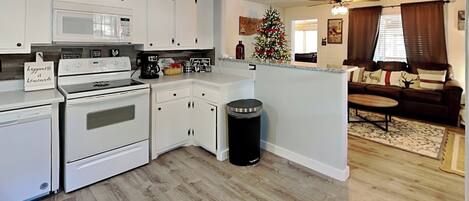 A modern kitchen with white cabinets, a microwave, and a stove. There is a trash can and a Christmas tree in the living area.