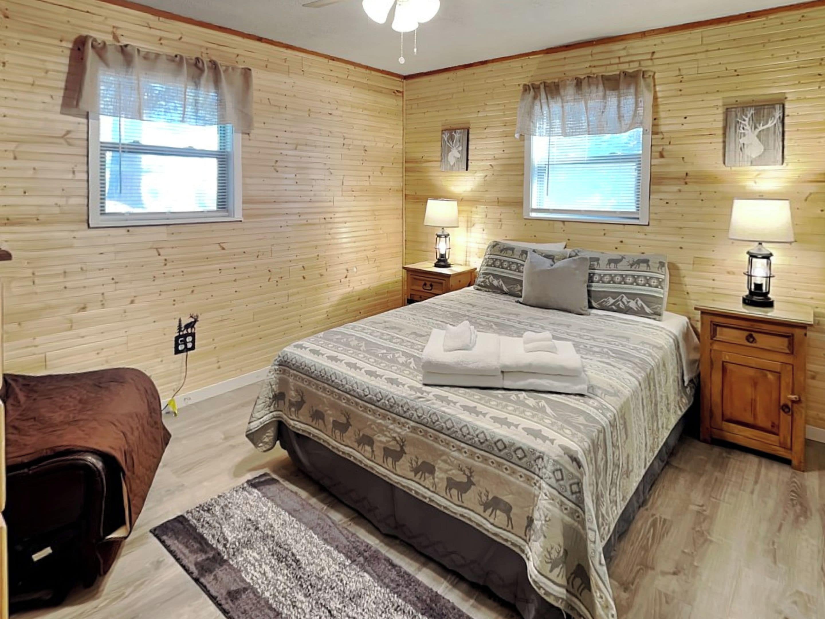 Una habitación acogedora con paredes de madera, una cama grande con ropa de cama estampada, dos lámparas de noche y una alfombra pequeña.