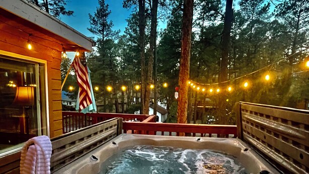 Un bain à remous entouré d’une terrasse en bois, avec un drapeau américain et des guirlandes lumineuses en arrière-plan.